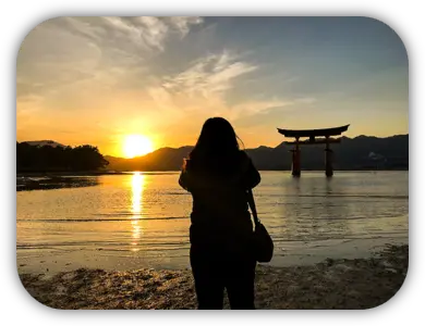 Silhueta de uma viajante diante do torii de Itsukushima ao pôr do sol