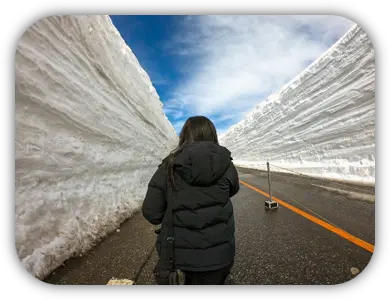 Viajante caminhando pela estrada entre paredes altas de neve em Tateyama Kurobe